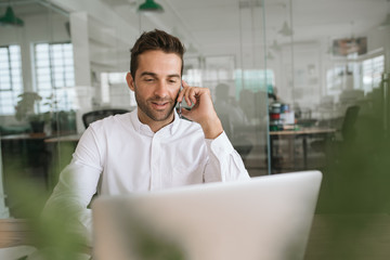 Smiling young businessman talking on a cellphone at work