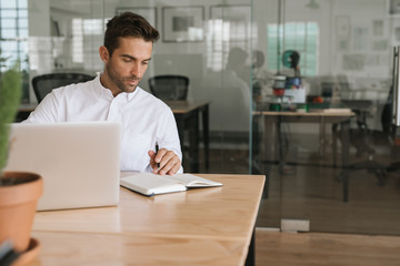 Young businessman working on a laptop and writing down notes