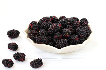 Blackberries are located in a plate on a white background