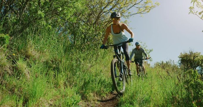 Summer mountain biking vacation, attractive couple riding mountain bikes together in the great outdoors in slow motion