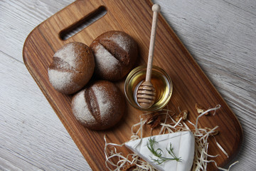 Top view of brie cheese with nuts, bun and honey on a wooden board and dark background. The concept of still life. Space for text