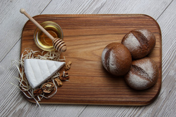 Top view of brie cheese with nuts, buns and honey on a wooden board and dark background. The concept of still life. Space for text