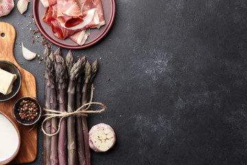 Bunch of fresh purple asparagus cooking with bacon, garlic and spices on rusty textured background