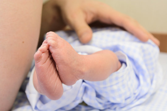 Small newborn baby feet in blue nappy with man hand