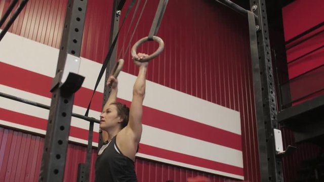 Young athletic woman is doing climb up on the gymnastic rings in sport gym