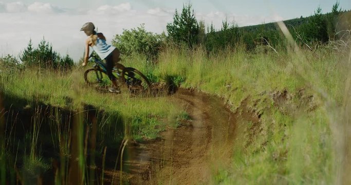 Summer mountain biking adventures, active adventurous woman riding her mountain bike around a berm turn in slow motion
