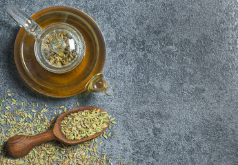 Herbal infusion fennel tea in glass tea pot with dried fennel seeds in wooden shovel on grey rustic table. Herbal tea alternative medicine background concept. - obrazy, fototapety, plakaty