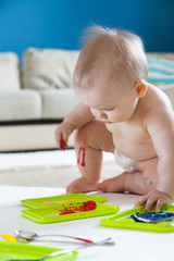 Baby child draws with colored paints hands, dirty feet. White list.