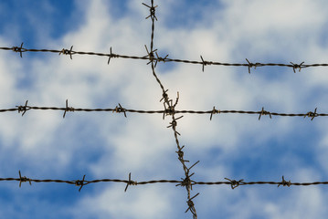 Barbed wire strands with azure sky and white clouds as background