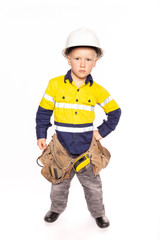 Young blond caucasian boy hand on hip role playing as an angry construction worker in a yellow and blue hi-viz shirt, boots, white hard hat, tool belt, a hammer and tape measure.