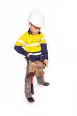 Young blond caucasian boy pointing down with a fierce look role playing a construction worker supervisor in a yellow and blue hi-viz shirt, boots, white hard hat, tool belt, a hammer and tape measure