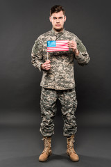 serious man in military uniform holding american flag on grey