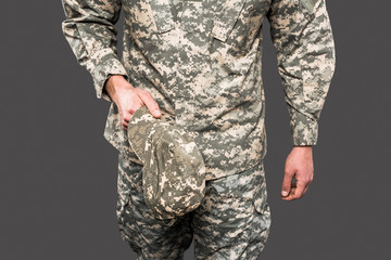 cropped view of soldier holding cap isolated on grey