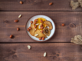 Fruit chips without sugar and additives on a small plate and peanuts, the plate is on a wooden tray, for a healthy snack to people leading a healthy lifestyle