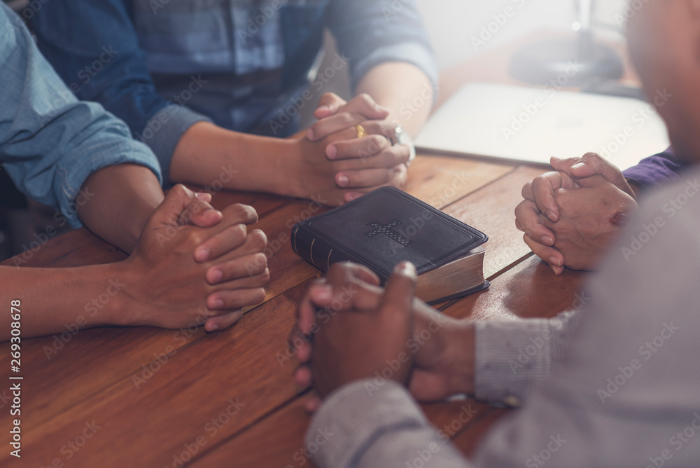 Wall mural Christians and Bible study concept. Group of discipleship Studying the Word Of God in church and christians holding each others hand praying together