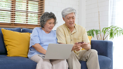 Fototapeta premium Senior asian couple shopping online by using laptop computer and credit card at home living room, Retirement people technology lifestyle