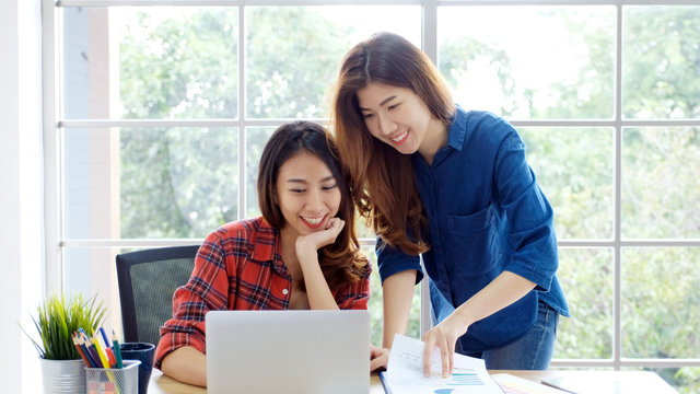  Two young asian women working with laptop computer at home office with happy emotion moment, working at home, small business, office casual lifestyle concept
