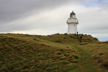 White beautiful lighthouse on a green grassy hill in the cloudy day. Waipapa point, South Island,...