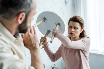 selective focus of offended woman holding chair and looking at scared man at home