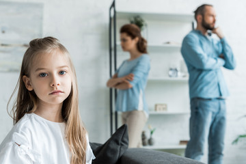 selective focus of sad kid looking at camera near quarreling parents at home