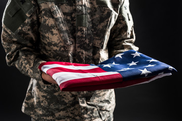 cropped view of man in military uniform holding flag of america isolated on black