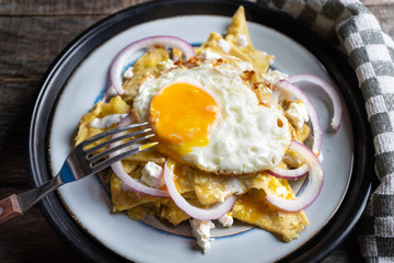 Mexican food: tasty green chilaquiles with fried egg, onion and fresh cheese