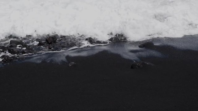 closeup slow motion capture of waves breaking on black sand beach in hawaii