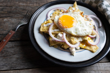 Mexican food: tasty green chilaquiles with fried egg, onion and fresh cheese