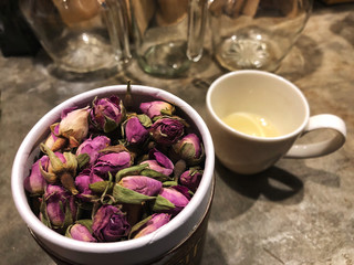 Pink Rose tea in package and white cup on the cement table with cafe light and glass bottle background.