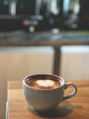 Heart love Latte art coffee in white cup on vintage wooden table with coffee machine background . Dark light and vintage style.