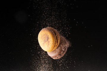 Two macaroons levitate with cocoa powder on a black background.