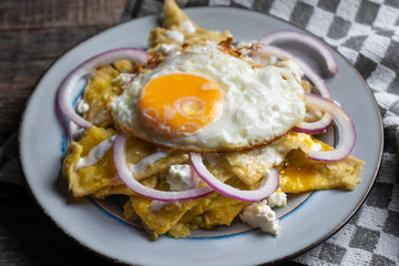 Mexican food: tasty green chilaquiles with fried egg, onion and fresh cheese