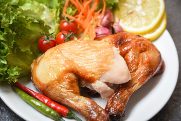 Roasted chicken legs on white plate with lemon chilli spicy herbs spices and salad lettuce vegetable