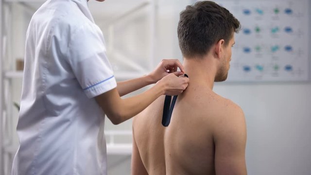 Physician applying Y-shaped tapes on patient upper back, reduce muscle tension