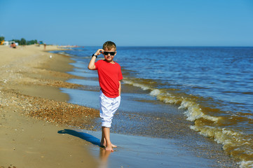 Beautiful boy posing on the coast . The child wears light jeans and a red t-shirt