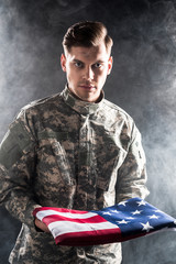 handsome man in military uniform holding american flag on black with smoke