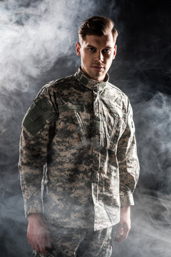 handsome man in military uniform looking at camera on black with smoke