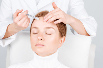 Woman is getting injection in forehead. Anti-aging treatment and face lift. Facial skin lifting injection to woman's face.