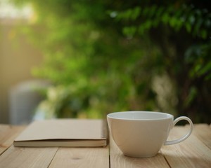 Cup of hot coffee, reading a book on wooden table in the green garden this morning. 