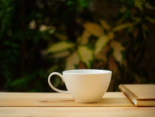 Cup of hot coffee, reading  a book on wooden table in the green garden this morning. 