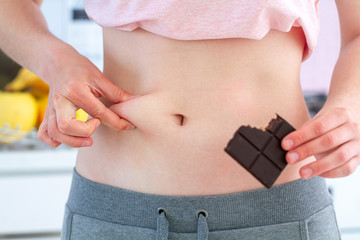Woman pinching excess fat on her waist and gaining extra pounds because of unhealthy junk carbs...