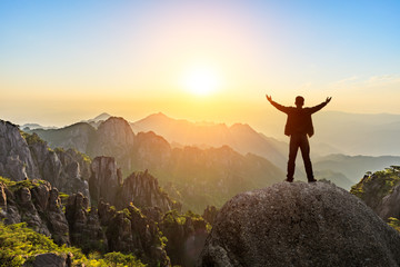 Hiker is standing on a rock with raised hands and enjoying sunrise - Powered by Adobe