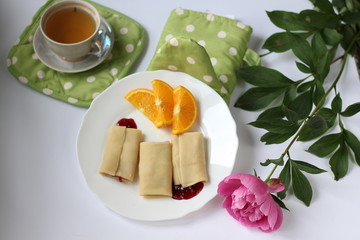 breakfast consisting of pancakes with berries and orange slices and a cup of tea