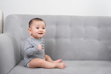 childhood, babyhood and people concept - happy little baby girl sitting on sofa at home