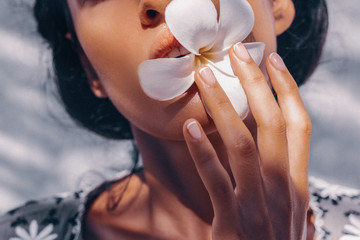 close up of beautiful young woman holding frangipani flower in mouth