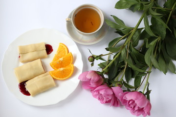 breakfast consisting of pancakes with berries and orange slices and a cup of tea