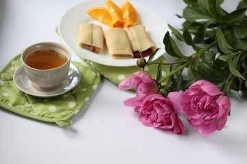 breakfast consisting of pancakes with berries and orange slices and a cup of tea