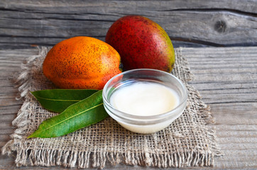 Mango body butter in a glass bowl and fresh ripe mangoes on old wooden table.Spa,organic cosmetic...