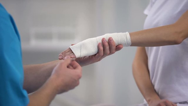 Orthopedist applying wrist elastic wrap on female patient hand joint dislocation