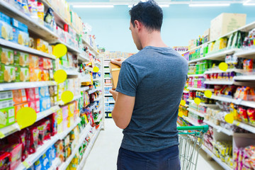 Unrecognizable caucasian man in grocery shop holding food box and look on it. Choosing goods in...